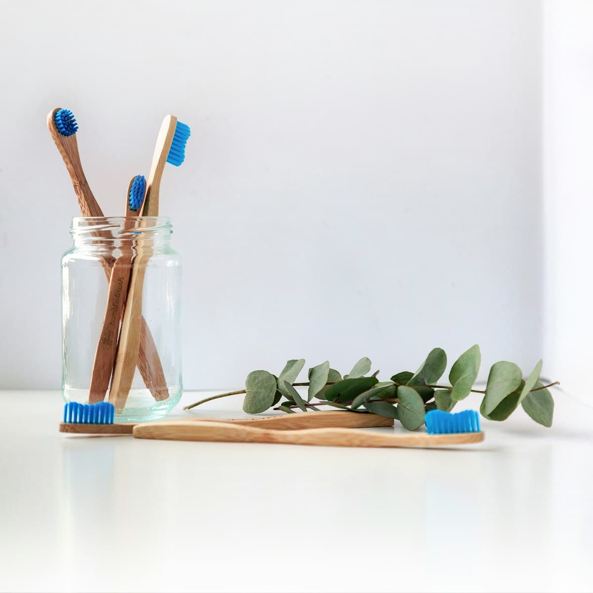 Bamboo toothbrushes in a glass jar beside green leaves